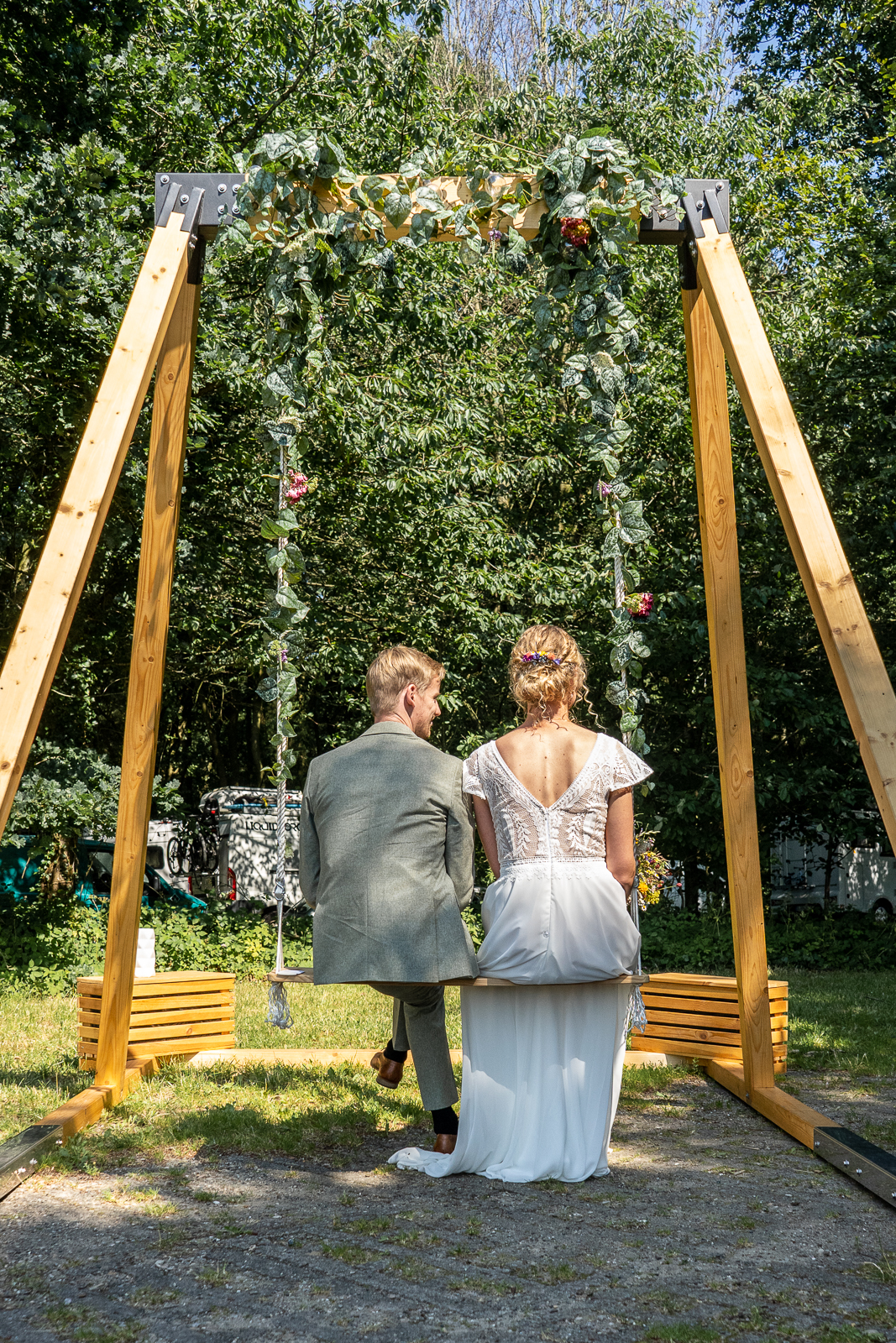 Brautpaar sitzt auf Hochzeitsschaukel mit Blumendeko im Grünen