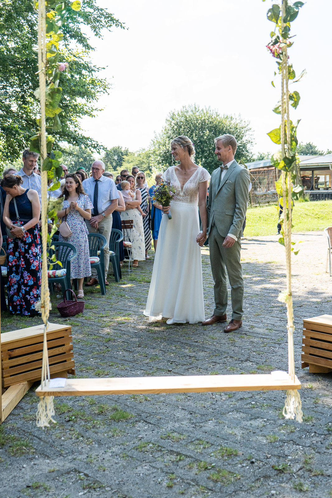 Brautpaar sitzt auf Hochzeitsschaukel mit Blumendeko im Grünen