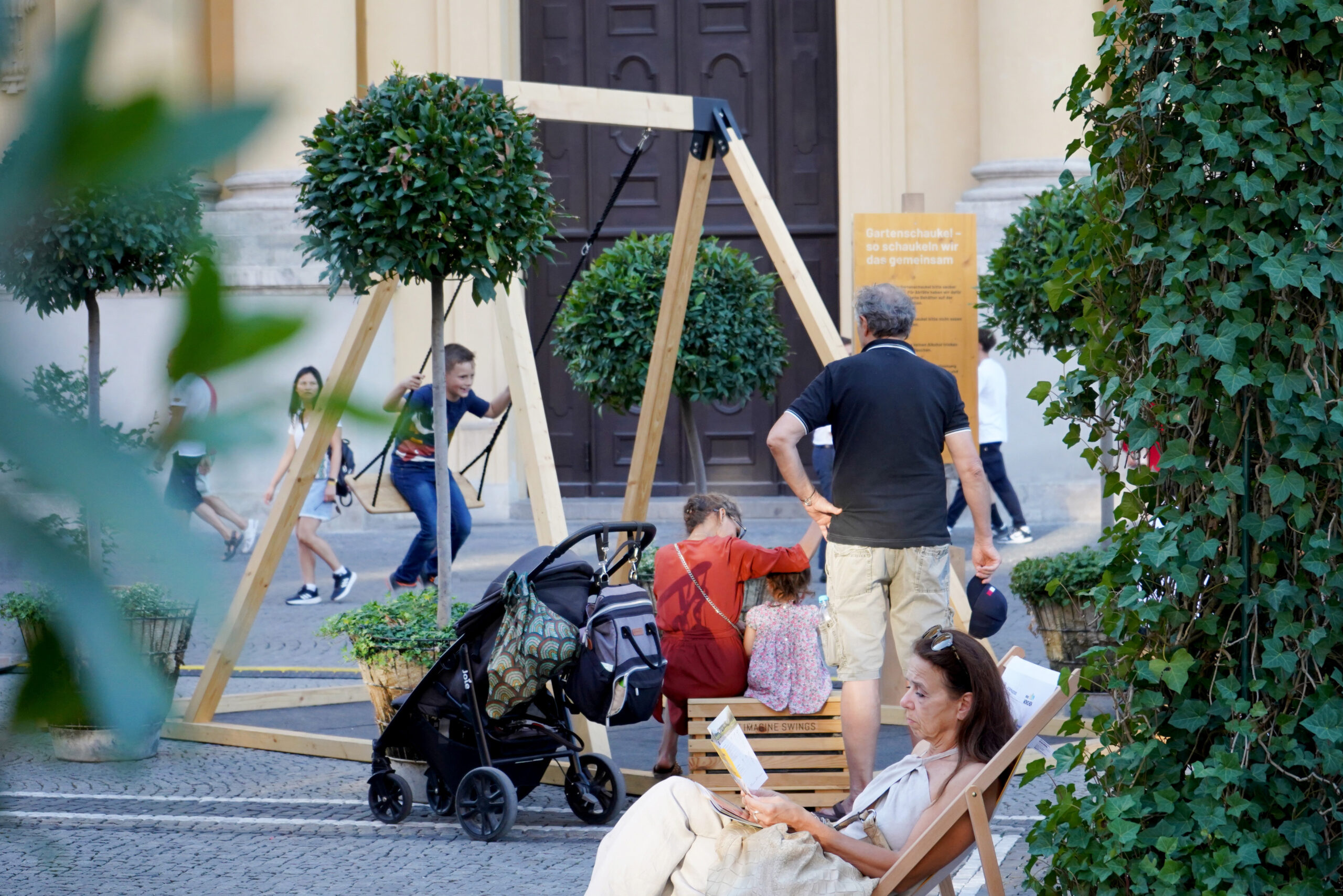 Imagine-Swings_Pop-up-Schaukel_IAA_Stadtoase_München-7 Schaukel auf einem Platz in der Stadt mit Begrünung und entspannten Menschen
