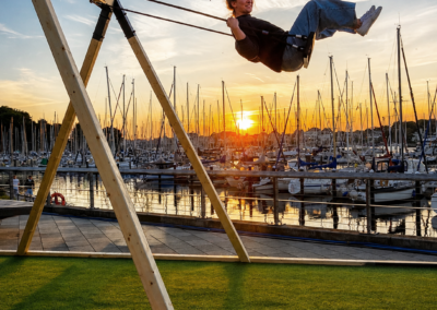 Frau schaukelt hoch über einen Sonnenuntergang am Hafen
